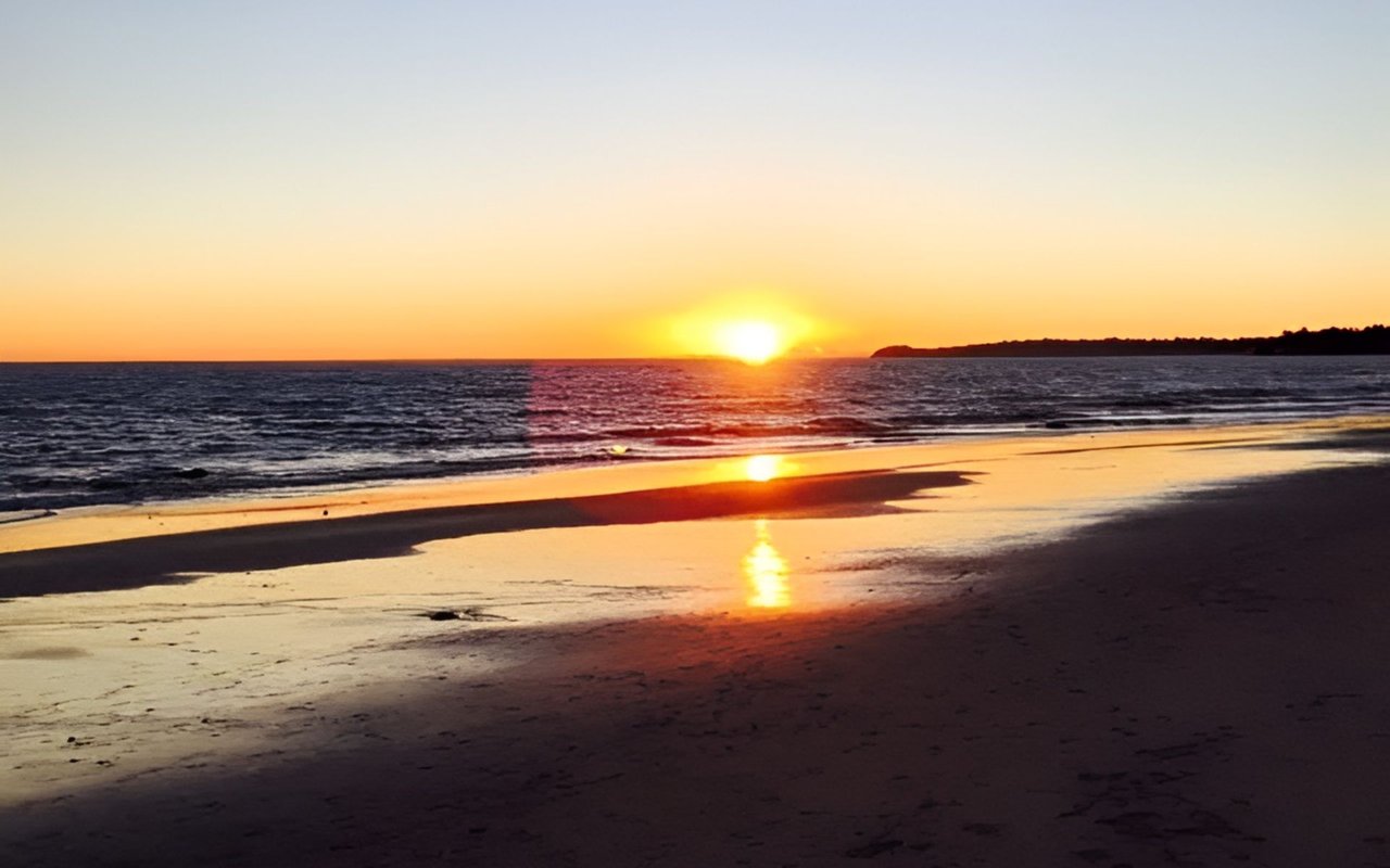 Beach at sunset with golden light reflecting on the shore and a distant headland.