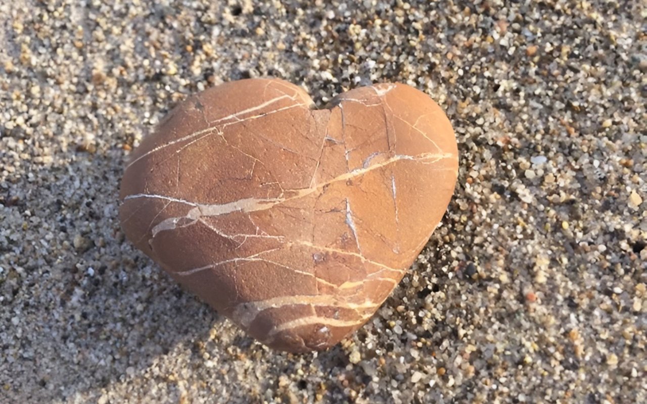 Heart-shaped reddish-brown stone with pale veins resting on coarse sand.