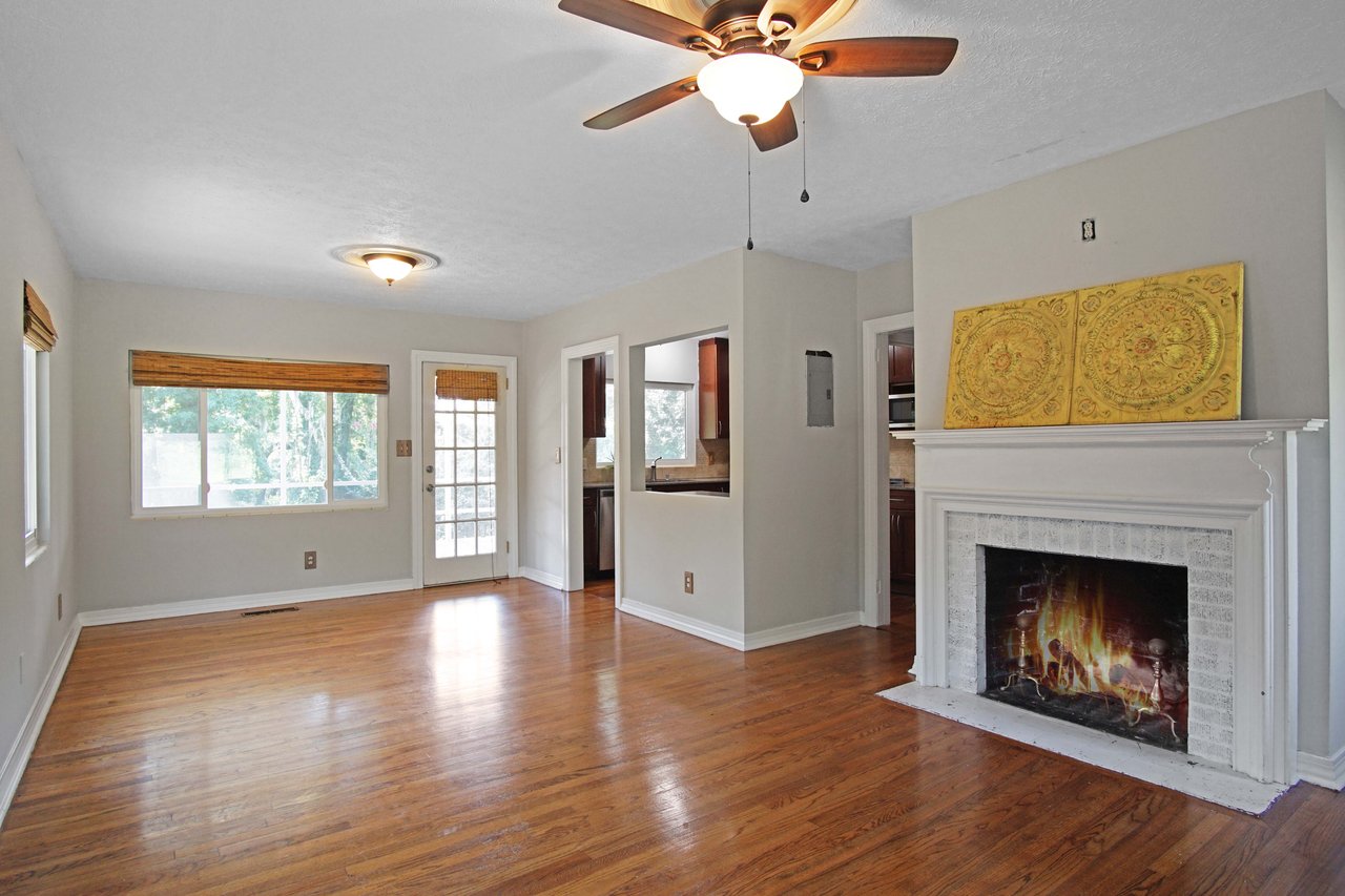 Spacious living area with hardwood floors, a lit fireplace, and a ceiling fan. Large windows and a glass door provide ample natural light.