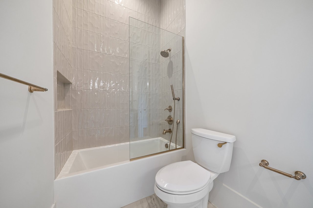 Bathroom with a tiled tub-shower, glass screen, recessed niche, bronze-tone fixtures, and white toilet.