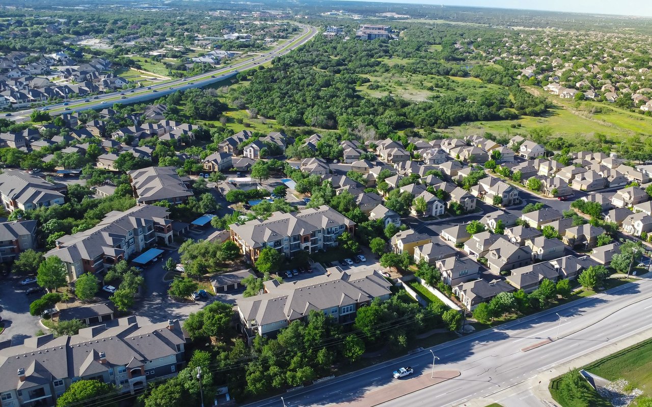 Aerial view of Cedar Park homes, with tree-lined green space and a highway in the foreground.