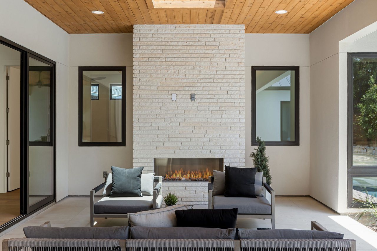 Covered patio at 1001 Bluebonnet Ln in Zilker, Austin, with a stone fireplace, wood-plank ceiling, and outdoor seating area.