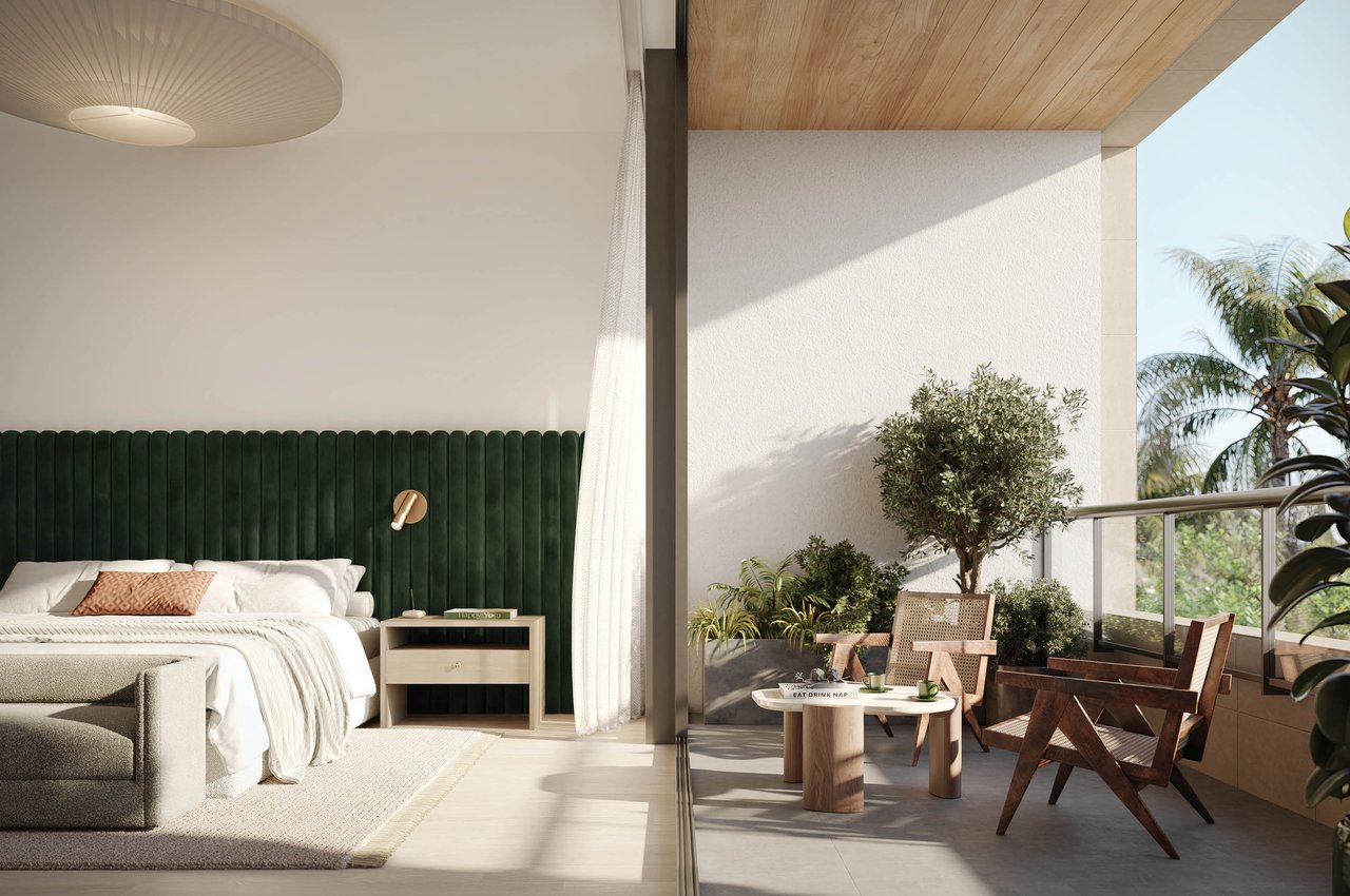 Bedroom with a deep green headboard and white bedding opening onto a furnished, sunlit balcony.