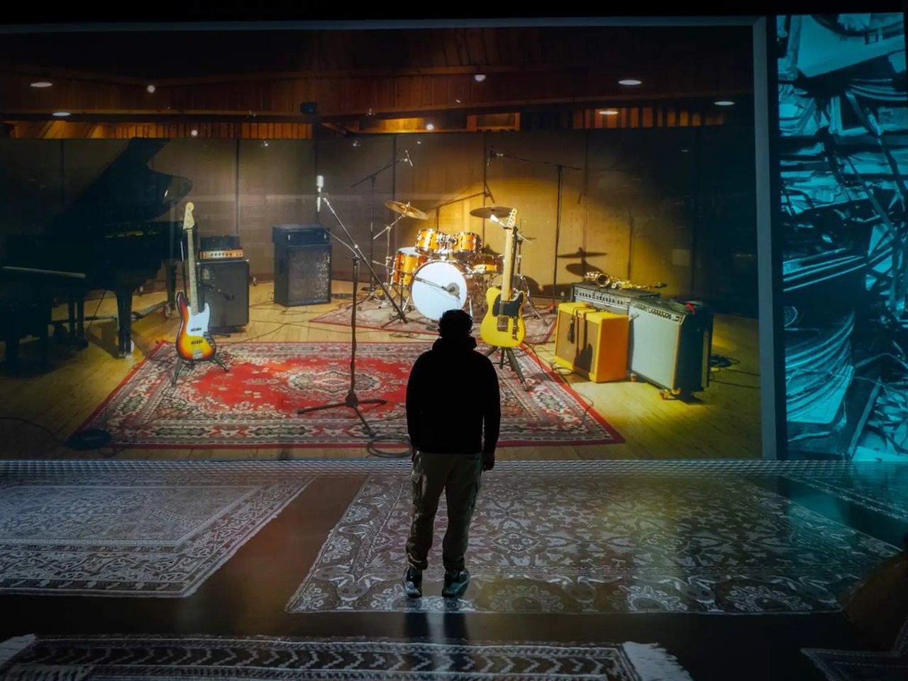 A visitor faces an immersive rock exhibit with guitars, amplifiers, and a drum kit.