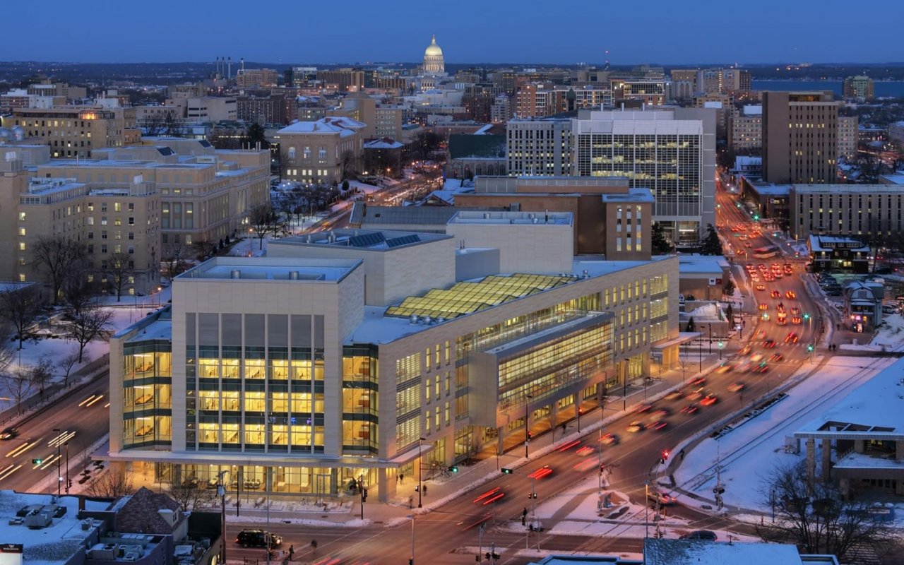 Downtown Madison at dusk, with the illuminated State Capitol above snowy streets and buildings.