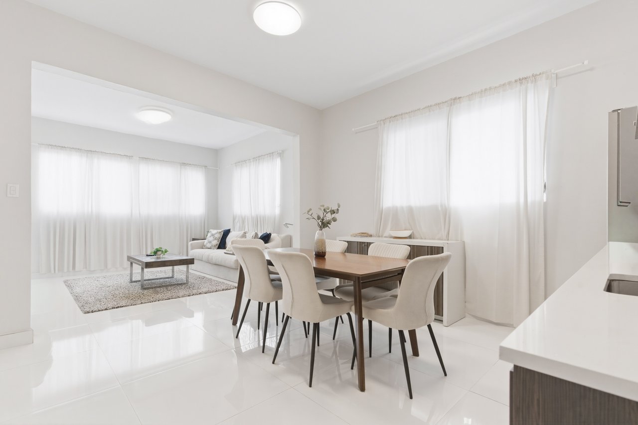 Dining and living area with a wooden table, cream chairs, and an adjoining white sofa.