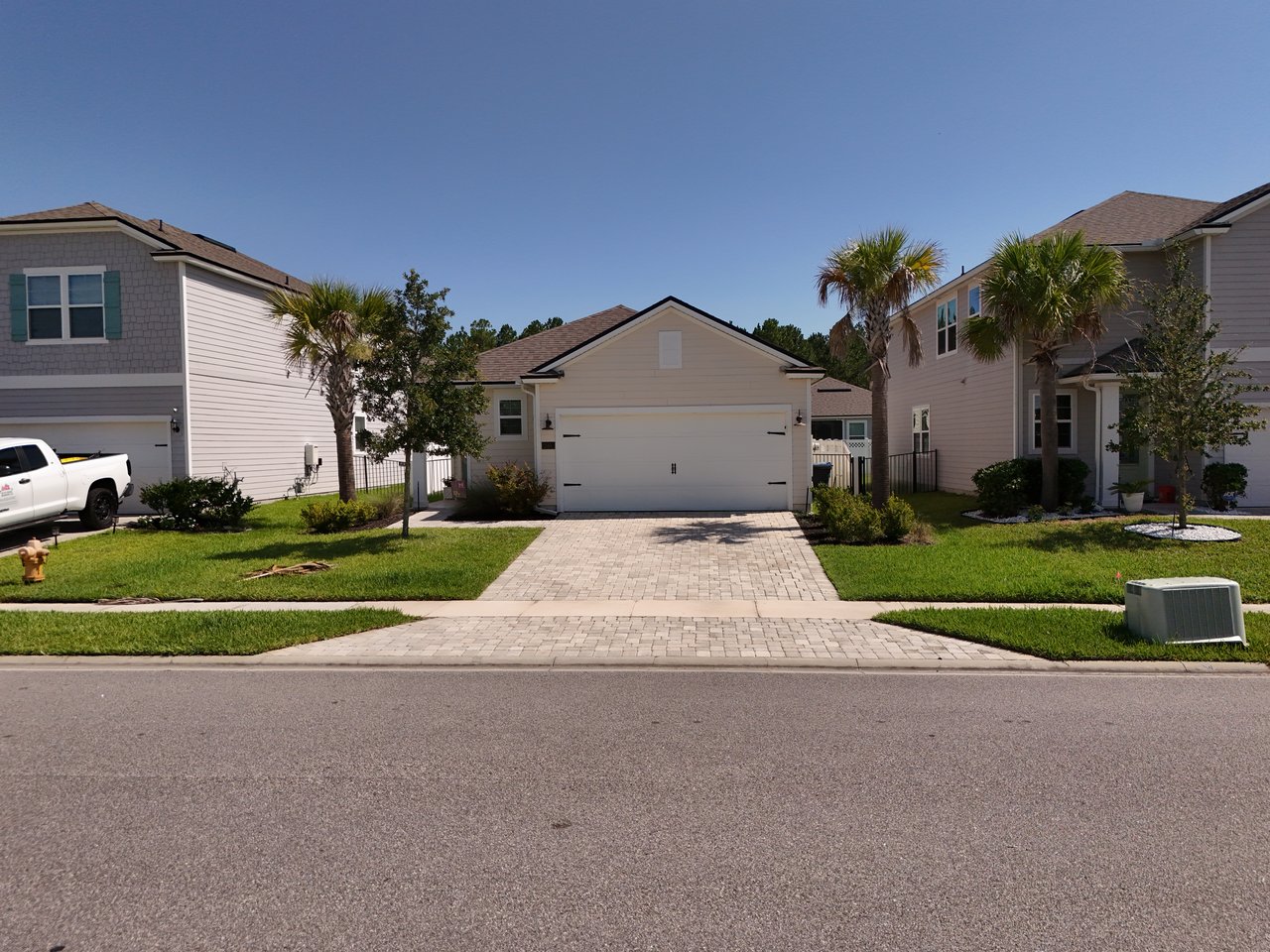 Light-colored home with a two-car garage, paver driveway, and landscaped front lawn.