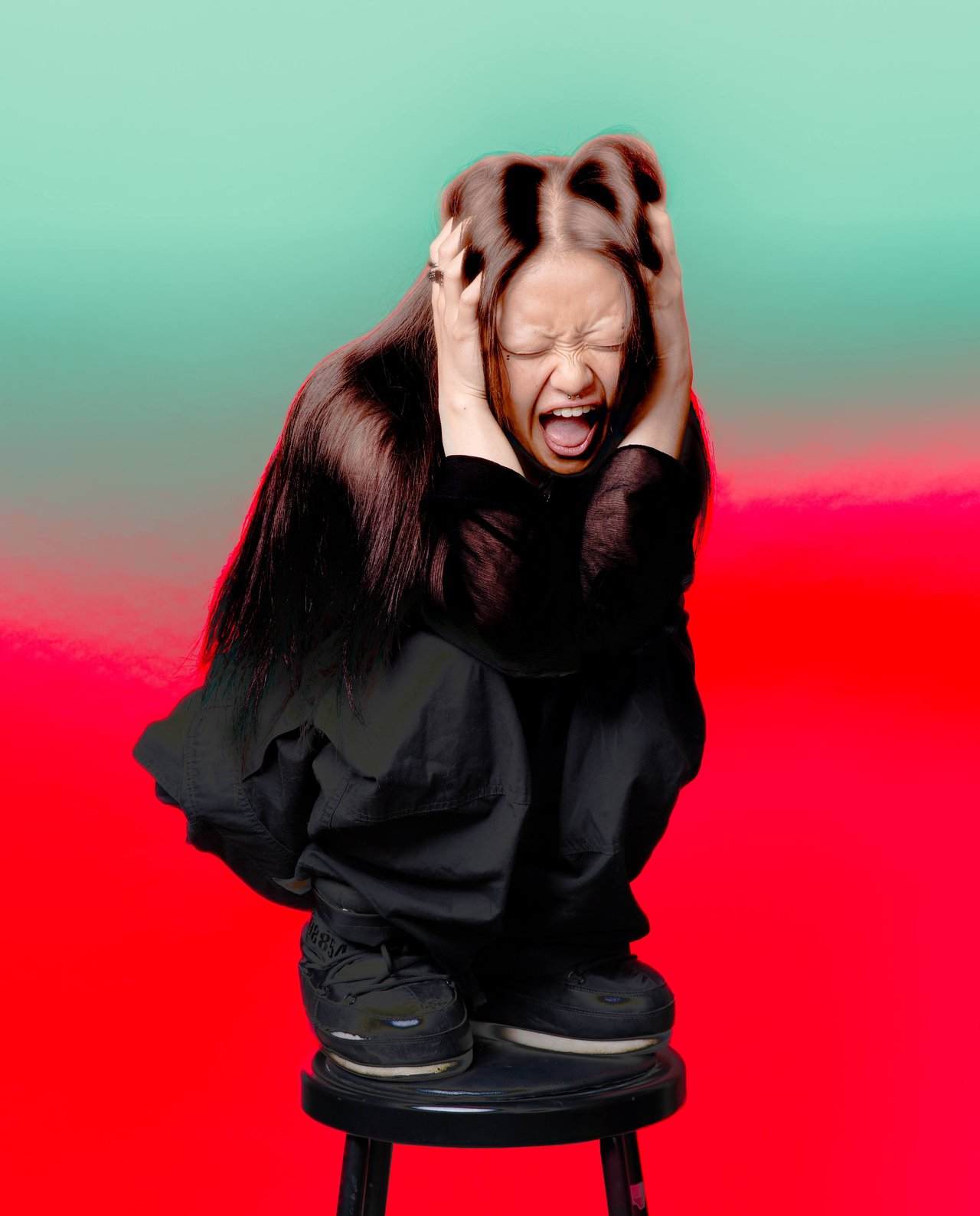 Dancer Jin crouches on a stool, eyes shut and hands gripping her head against a red and turquoise backdrop.