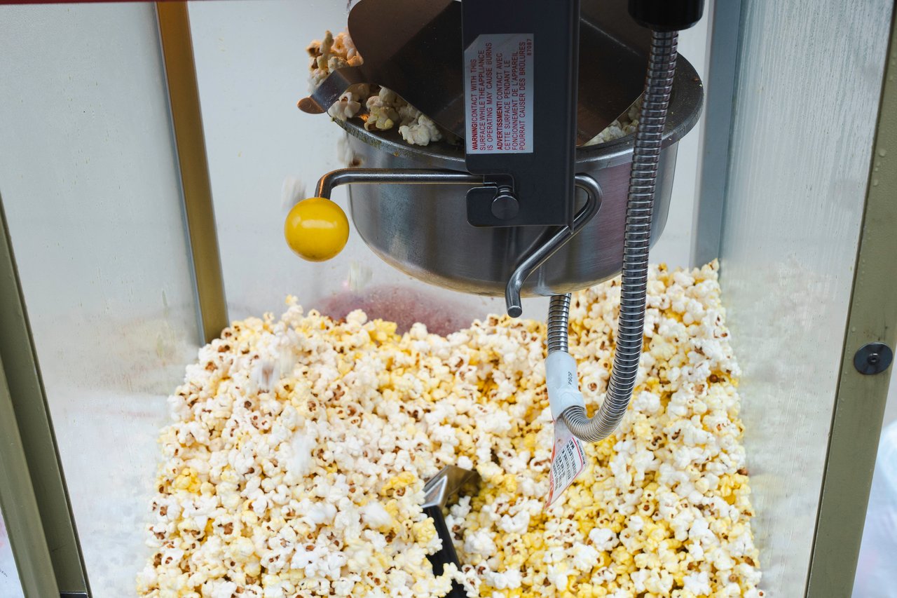 Fresh popcorn overflowing beneath the kettle of a commercial popcorn machine.
