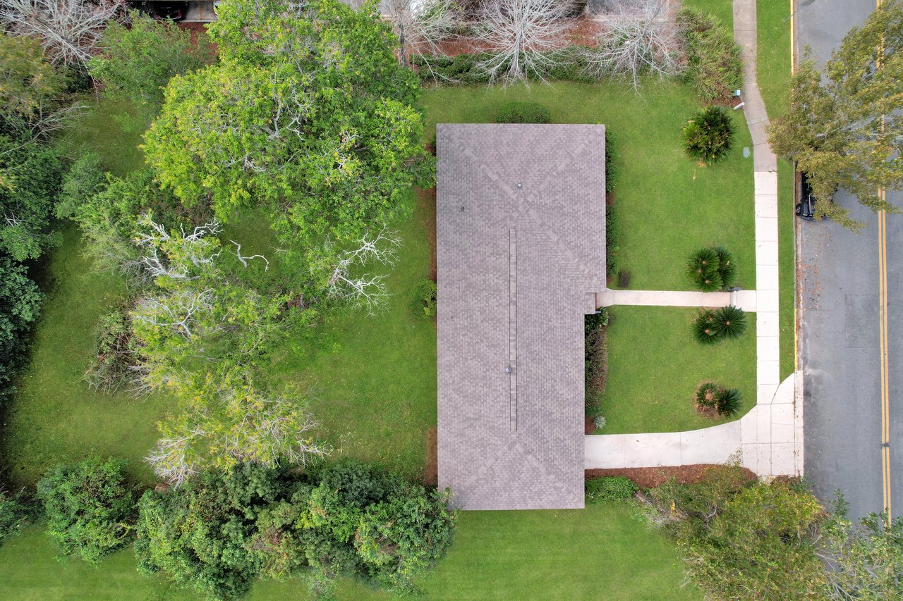 Aerial view of a house surrounded by lush trees and green grass, showcasing a serene residential landscape.