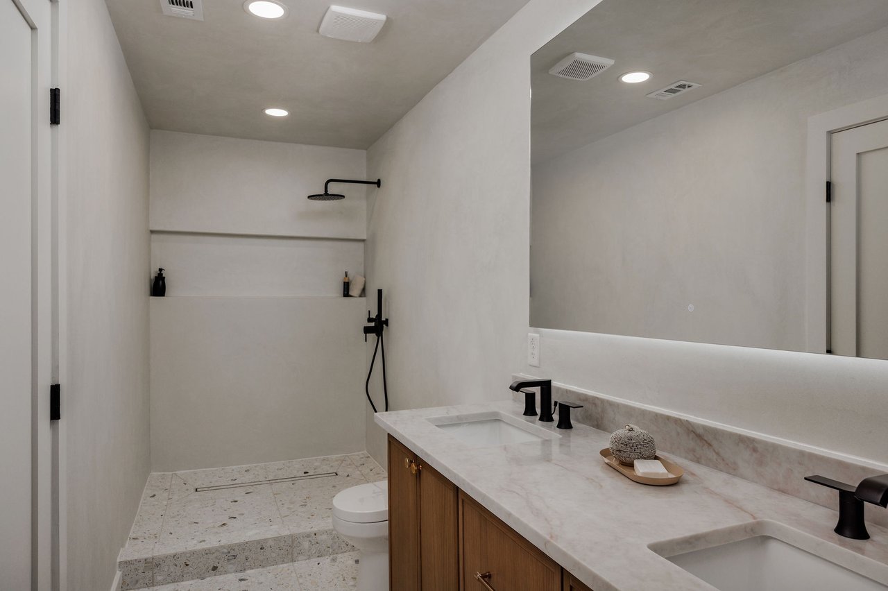 Modern bathroom with a walk-in shower, pale stone tile, and a double wood vanity.