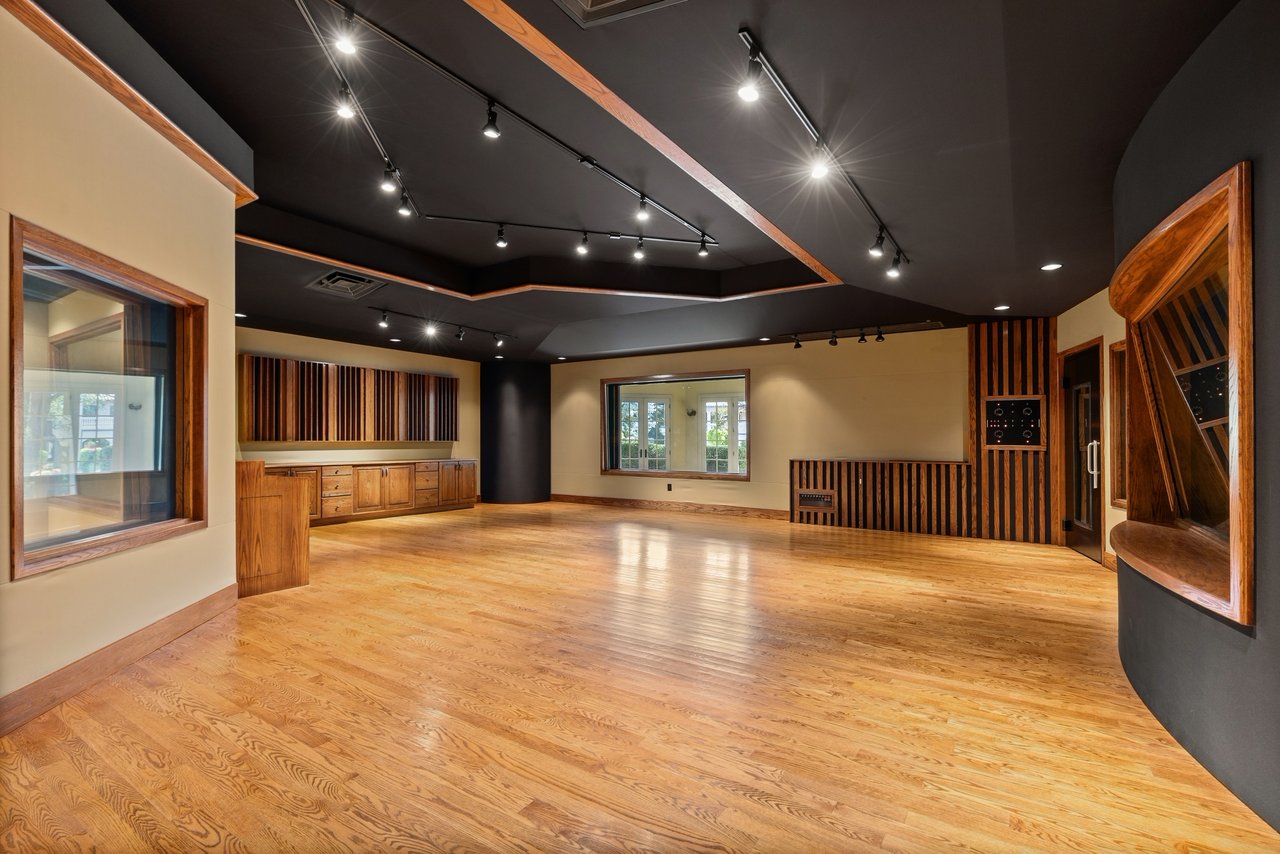 Vacant music studio with polished wood floors, acoustic wood slats, and a dark ceiling with track lighting.