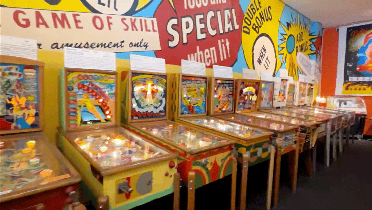 Row of colorful pinball machines beneath oversized arcade game signage.