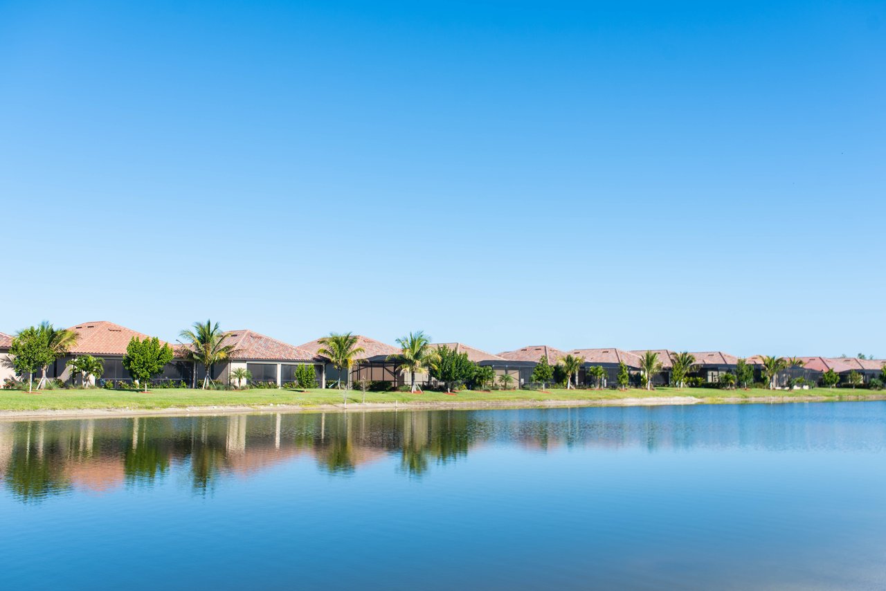 Lakefront homes with terracotta roofs and palm trees reflected in a calm lake.