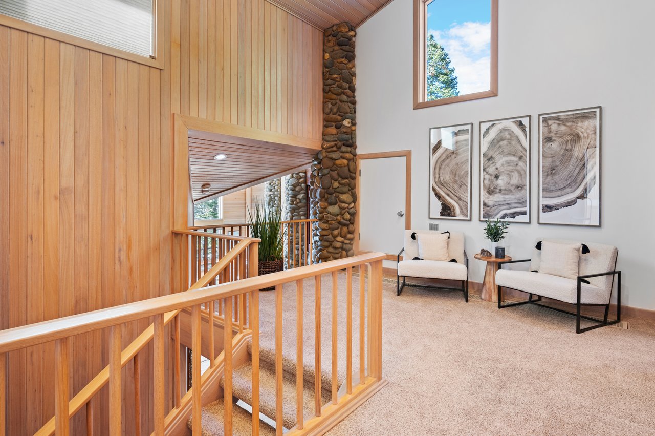 Upstairs landing with wood railings, a stone column, and two chairs beside the stairway.