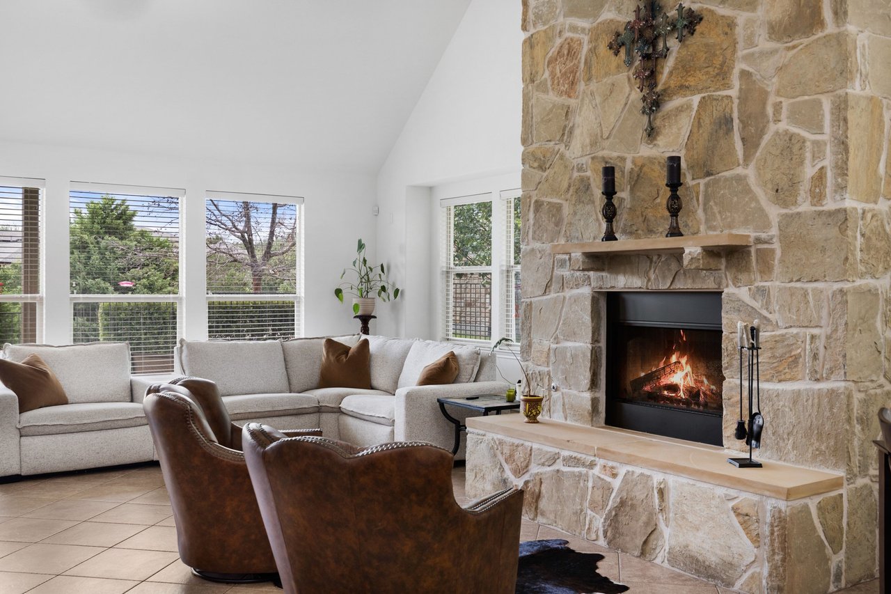 Living room with a stone fireplace, pale sectional sofa, and two brown leather chairs.