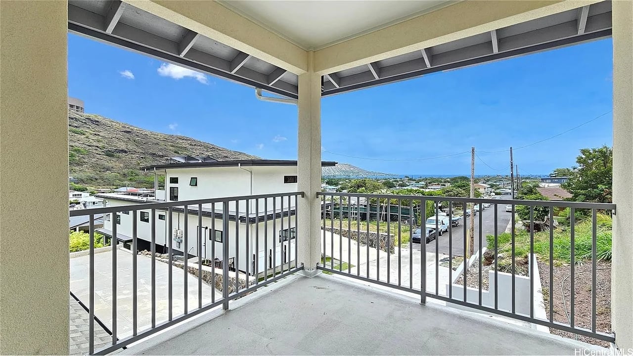 Covered balcony overlooking a neighborhood and hillside, with distant mountain ridges.