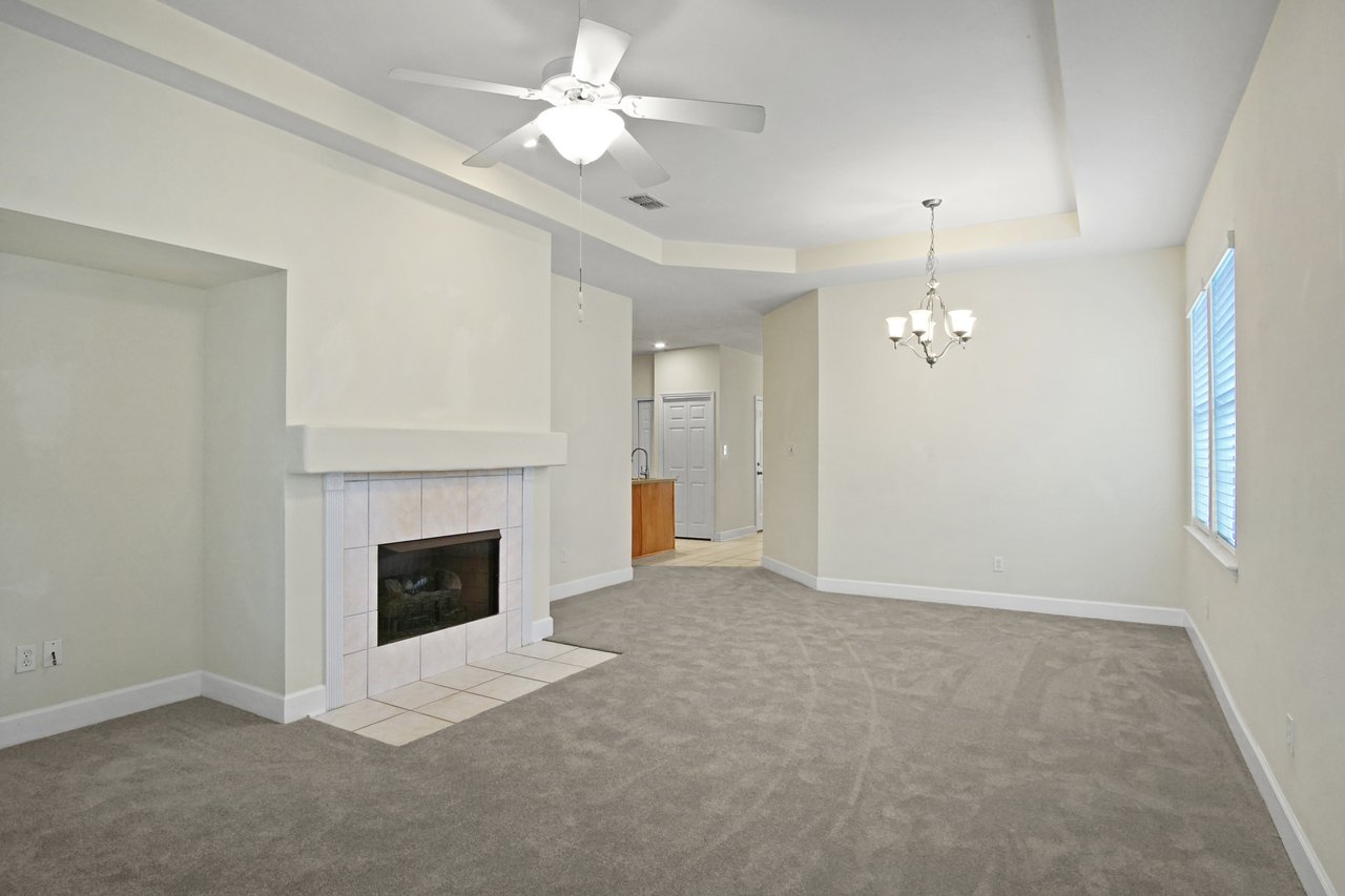 Living and dining area at 5441 Hampton Hill Circle, Tallahassee, Florida 32311 featuring fireplace, chandelier, and tray ceiling.