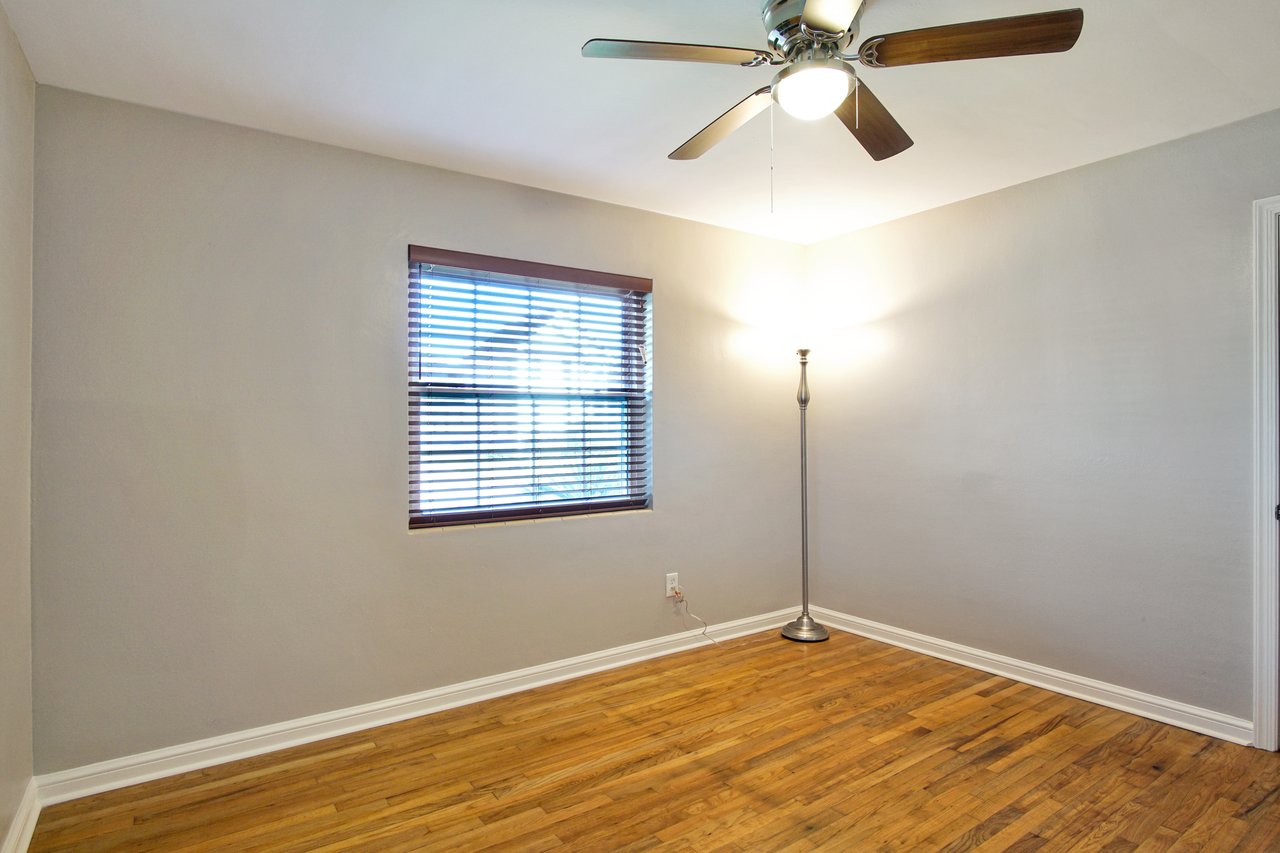 An empty room featuring hardwood floors and a ceiling fan, creating a spacious and airy atmosphere.