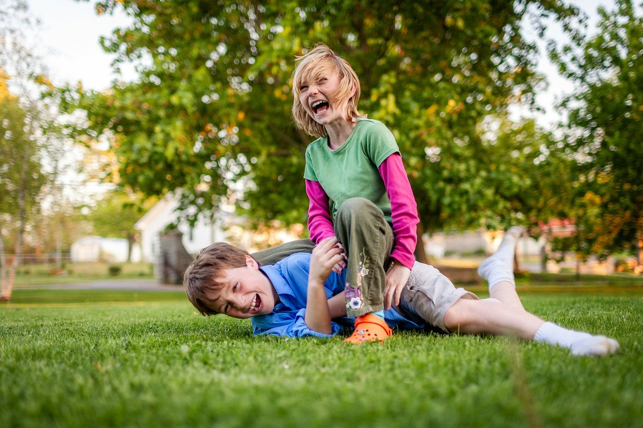 Two kids laughing and playing on a green front lawn in a family-friendly Montgomery County TX neighborhood