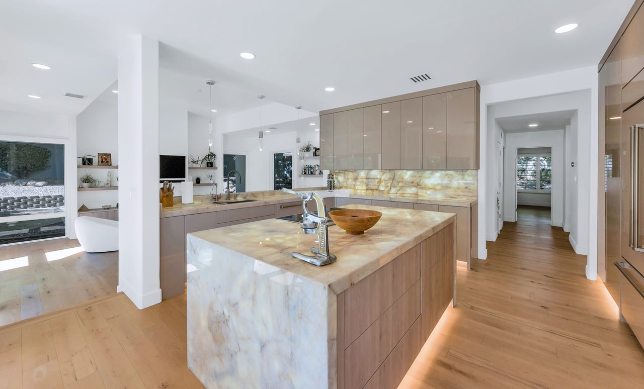 Contemporary kitchen with a large pale stone island and illuminated stone backsplash.
