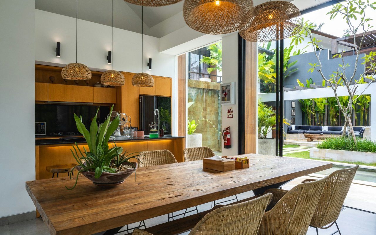 Open-plan kitchen and dining area with a rustic wood table, woven chairs and views of a tropical courtyard.