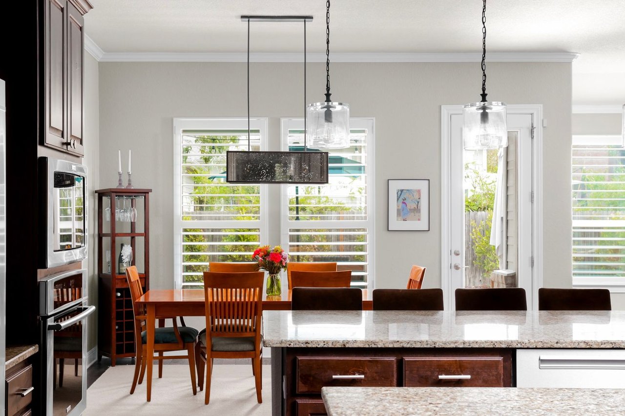 Kitchen with a granite island, dark wood cabinetry, and a dining table beside shuttered windows.