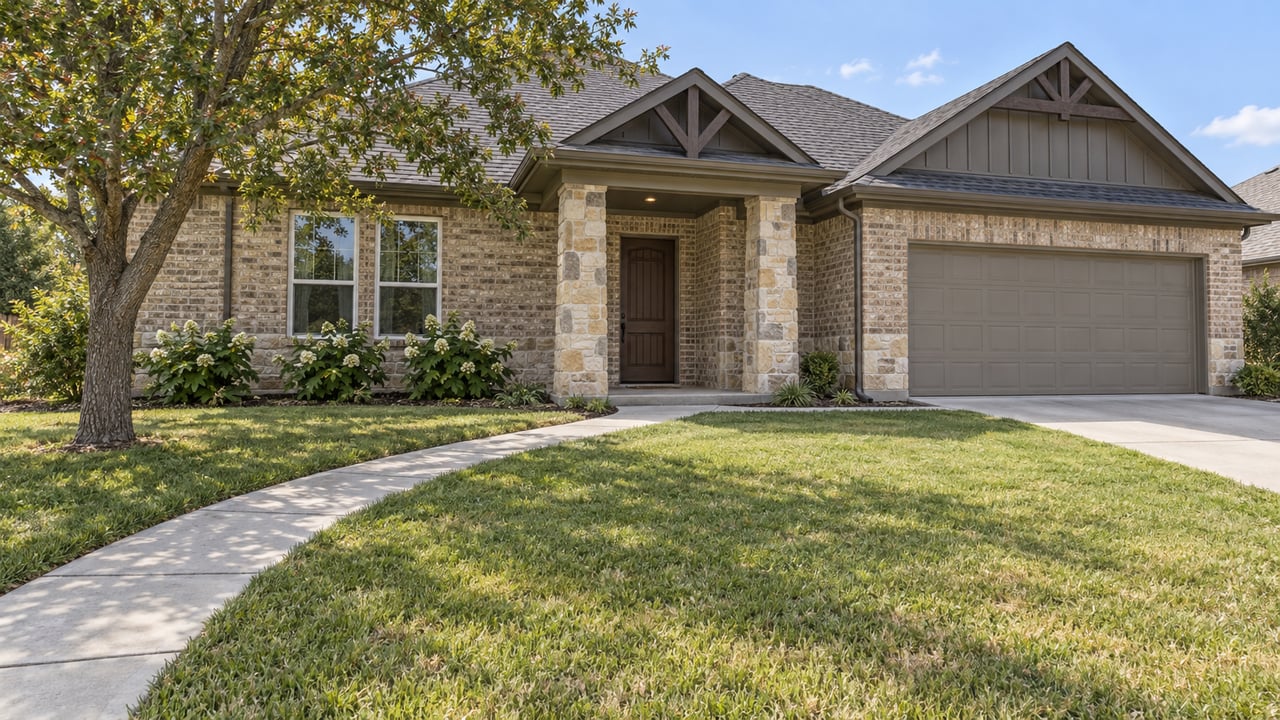 Brick-and-stone single-story home behind a broad lawn, with a concrete approach, shaded porch and attached garage.