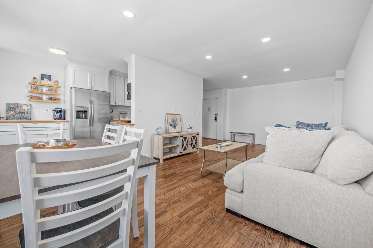 Open-plan living room with a light sofa, dining table, kitchen, and hardwood floors.