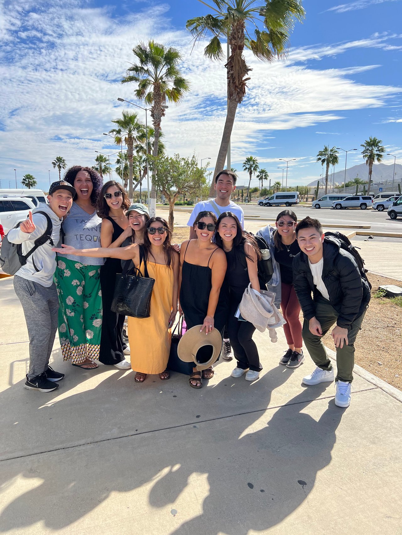 A group of colleagues pose together outdoors beneath palm trees on a sunny day.