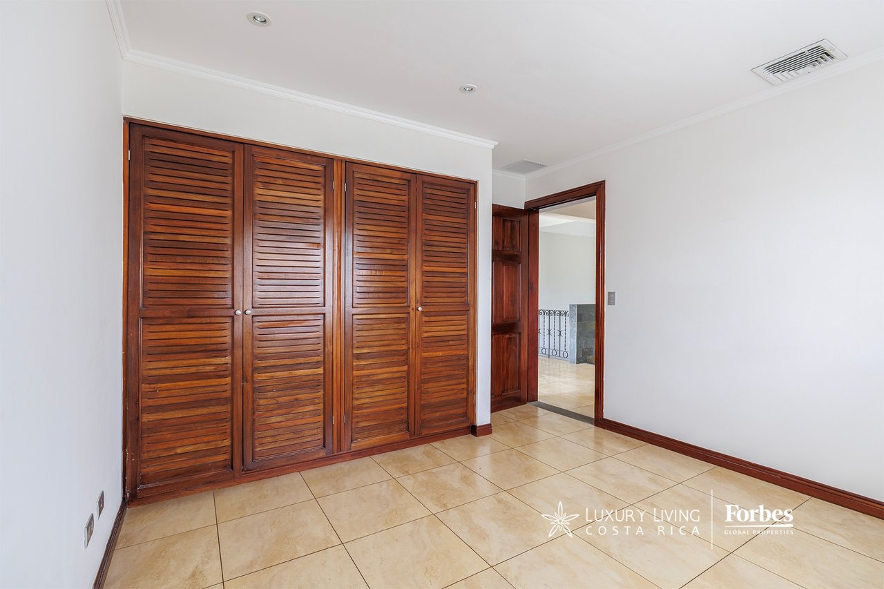 Empty bedroom with built-in wooden louvered closets and a beige tiled floor.