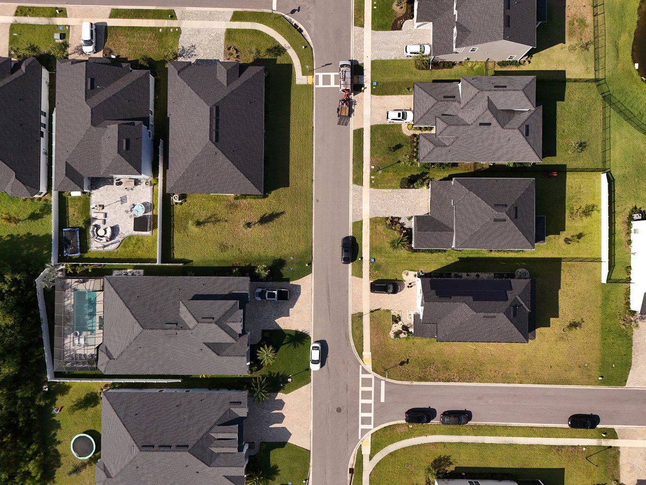 Aerial view of detached homes along a neighborhood street, including a backyard pool in a screened enclosure.