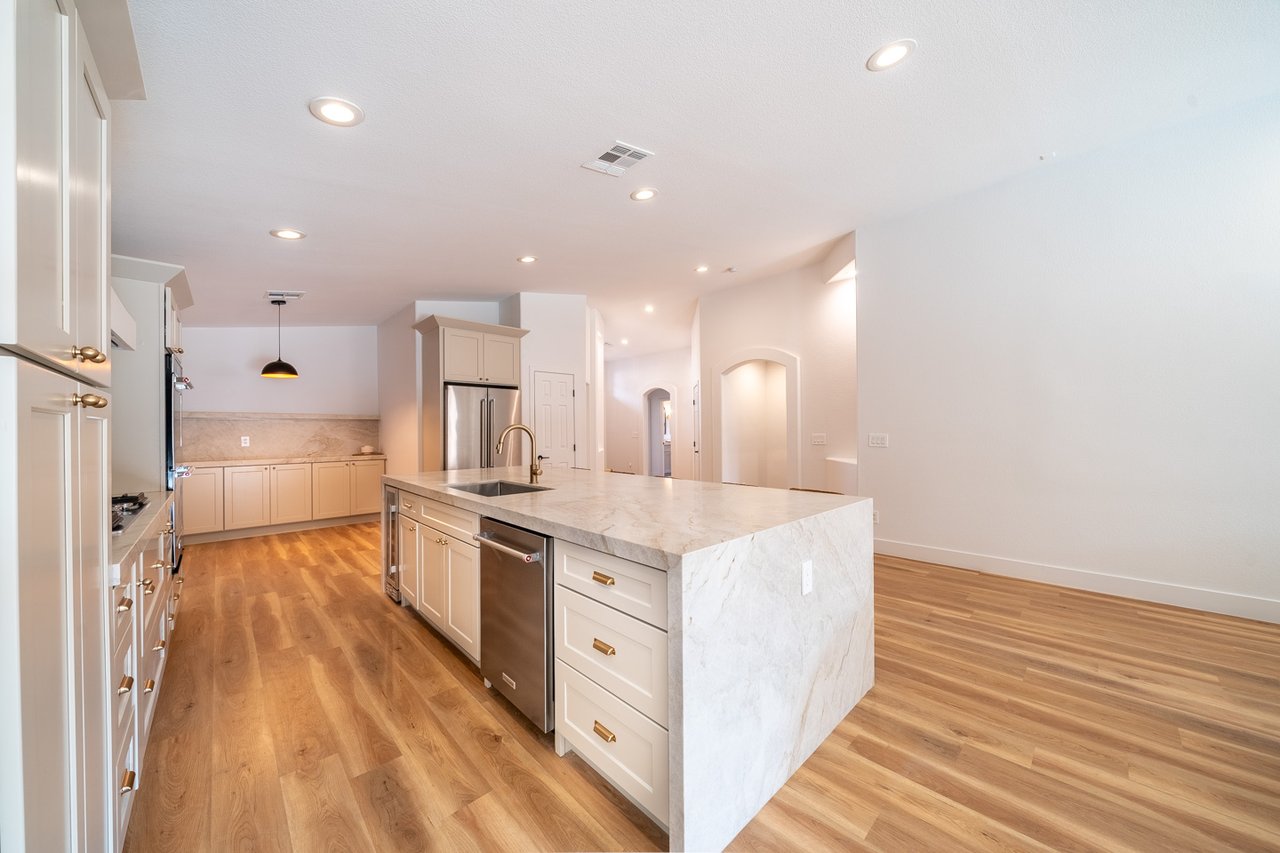 Kitchen with a large marble island, white cabinetry, stainless steel appliances, and wood floors.
