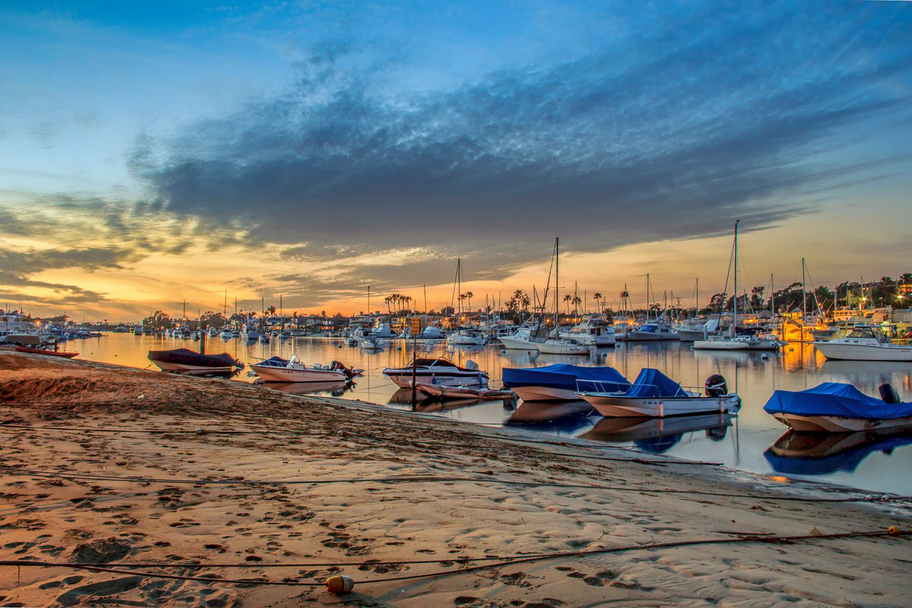 Boats moored along a sandy marina shoreline beneath dramatic dusk clouds.