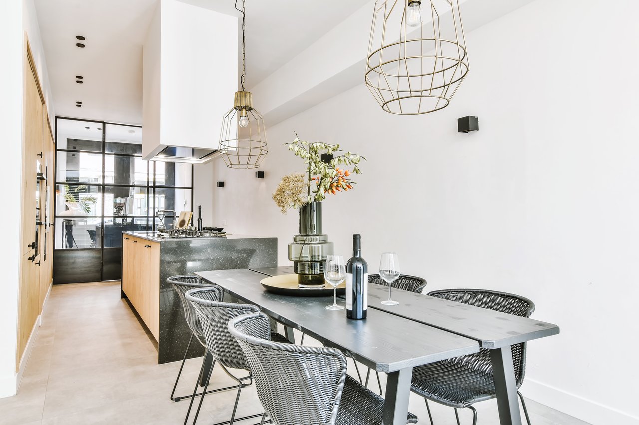 Modern kitchen and dining area with a dark stone island, woven chairs, and gold pendant lights.