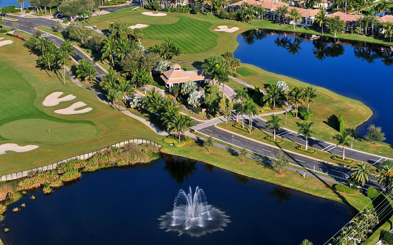 Aerial view of a golf course community with palm-lined roads and a fountain pond