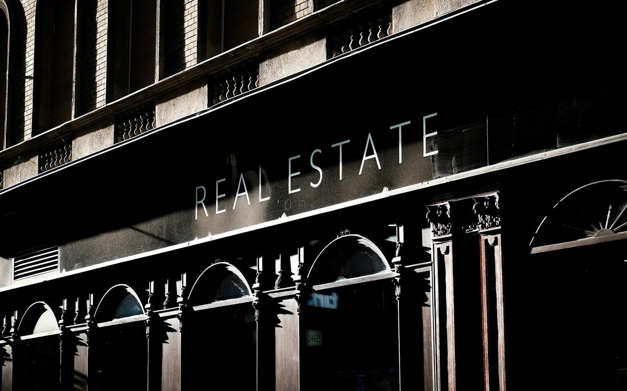 Real estate storefront sign on an ornate brick-and-stone building facade.