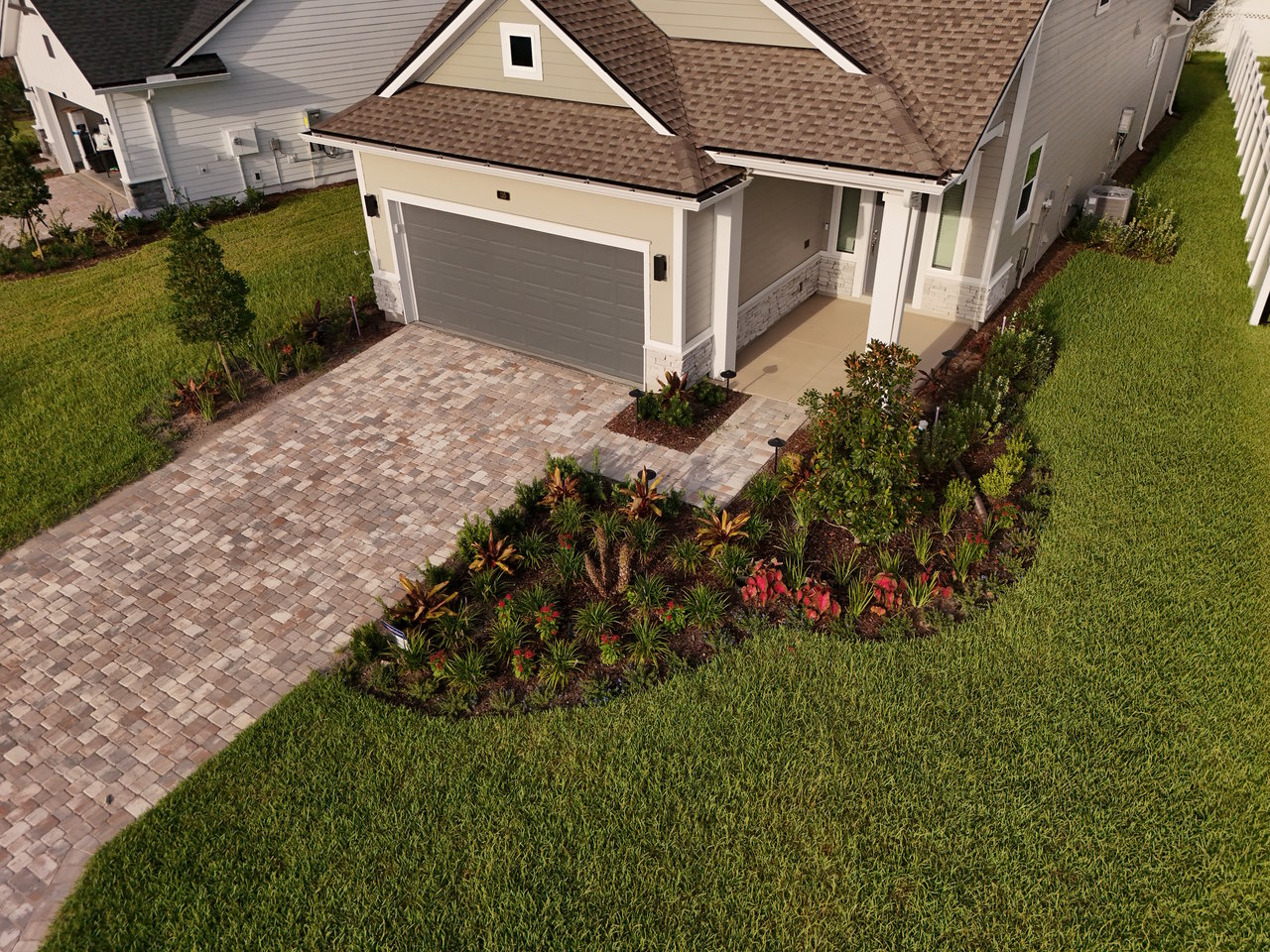 Home with a gray double garage, paver driveway, and landscaped front yard.