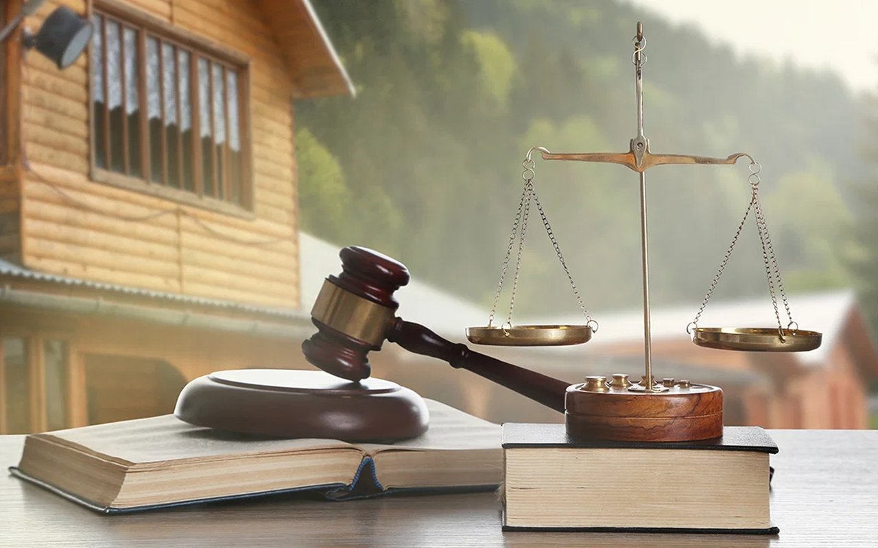 Gavel and balance scales on law books, with a wooden house in the background.
