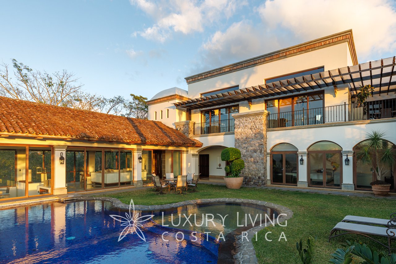 Luxury home with a blue swimming pool, tiled roof, stone accents, and covered terrace.