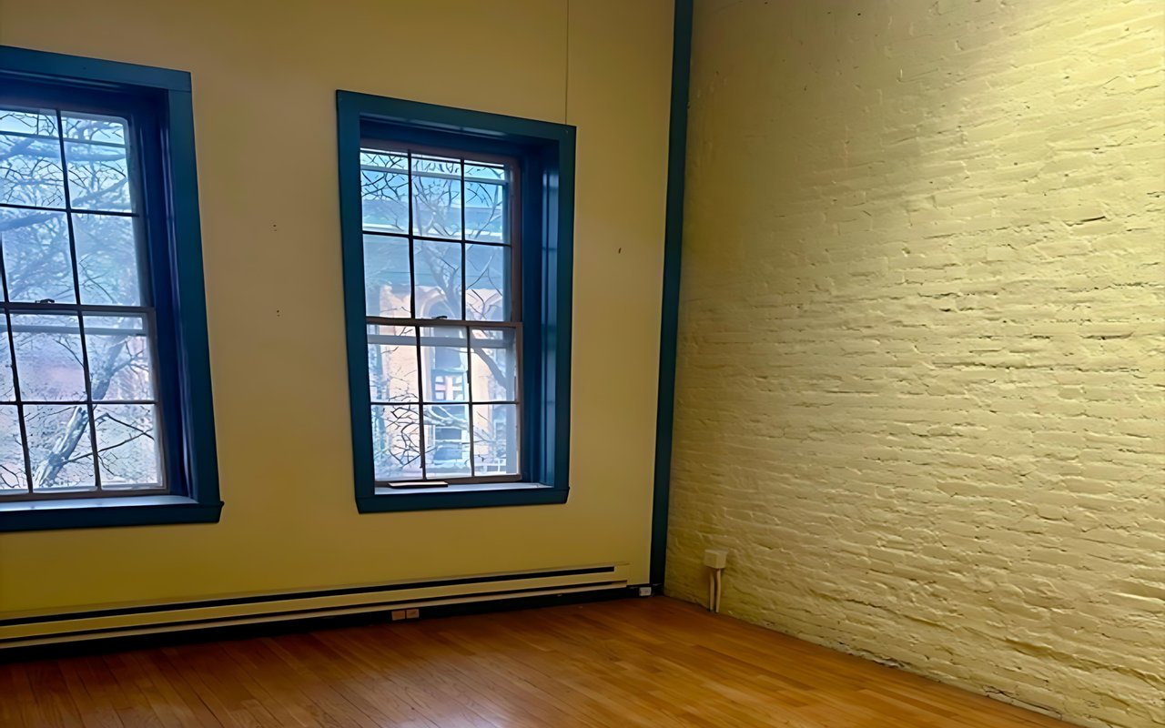 Vacant office with tall windows, a white brick wall, and hardwood floors.