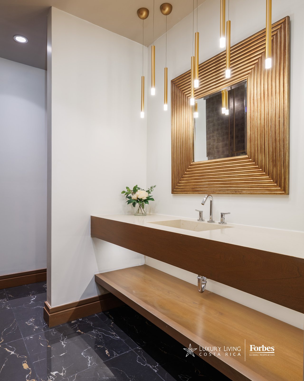 Bathroom vanity with a sculptural wood counter, gold pendant lights, and an oversized framed mirror.