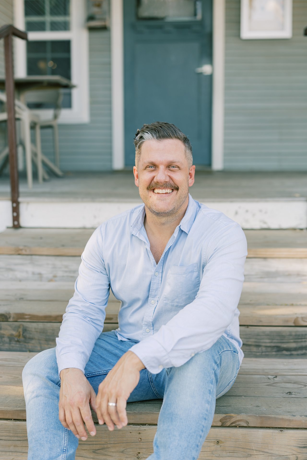 Cody Culberson smiling on porch steps in a light blue shirt and jeans.