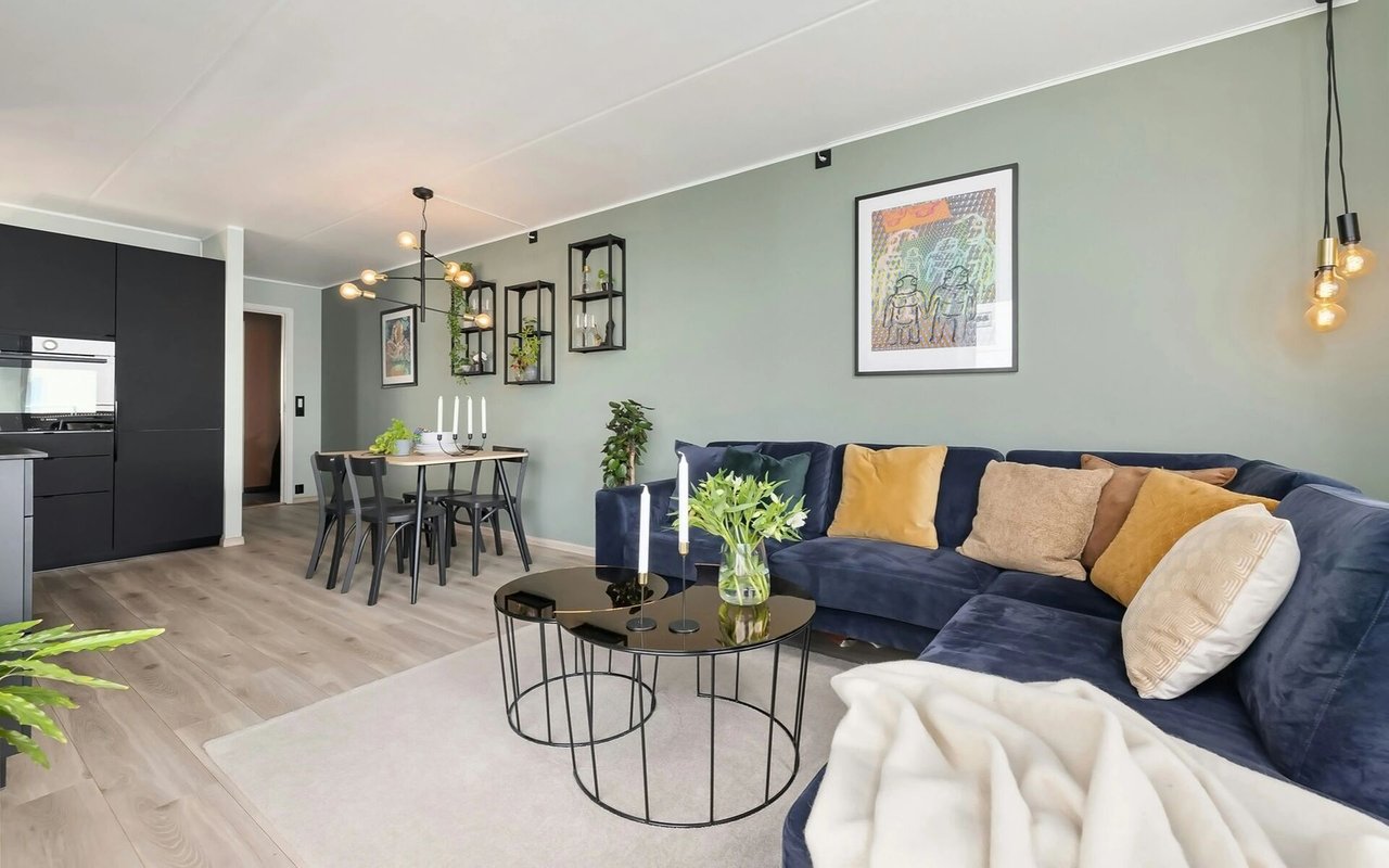 Open-plan living room with a navy sectional, nested coffee tables, dining area, and black kitchen cabinetry.