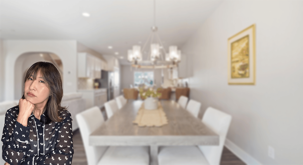 Woman resting her chin on her hand in front of a dining room and kitchen.