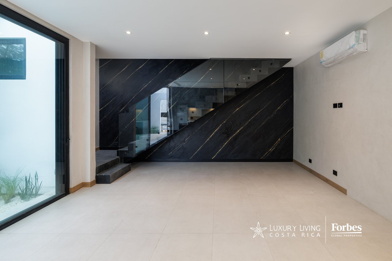 Vacant modern room with a striking black marble staircase and glass railing beside a planted courtyard.