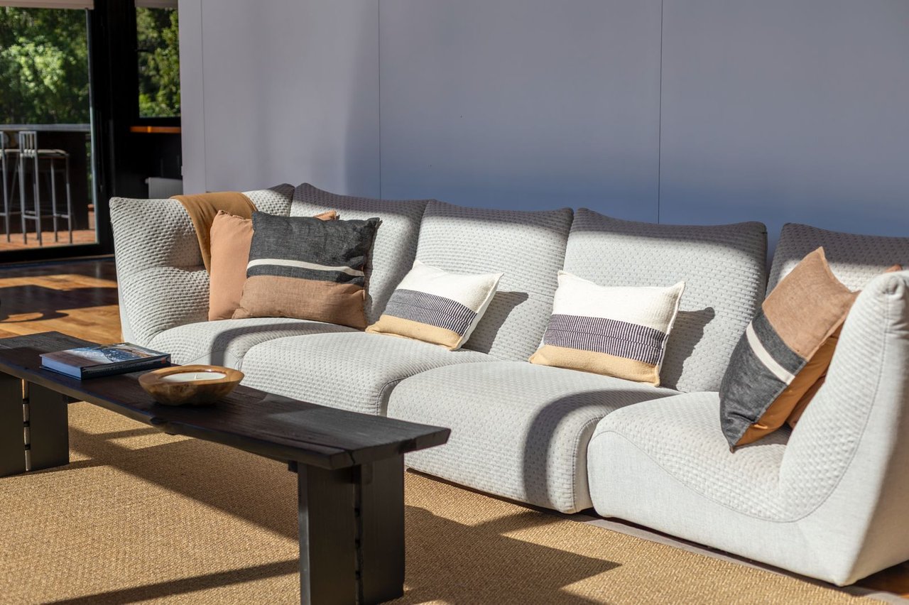 Living room with a light-gray sectional sofa, neutral pillows, and a dark coffee table in sunlight.