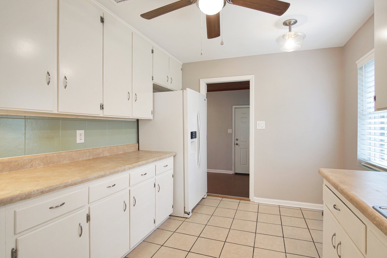 A bright kitchen featuring white cabinets and a ceiling fan, creating a clean and airy atmosphere.