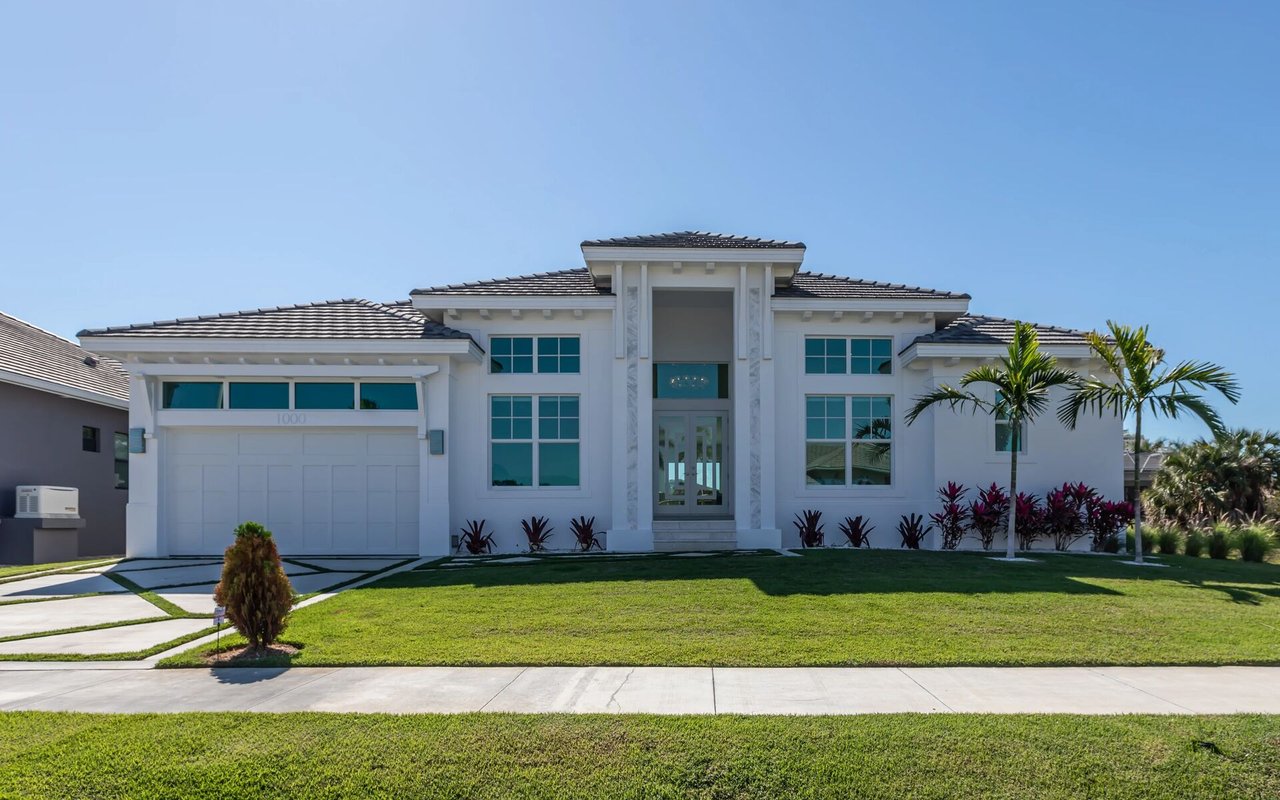 White modern home with a tall central entry, wide garage, palm trees, and a landscaped lawn.