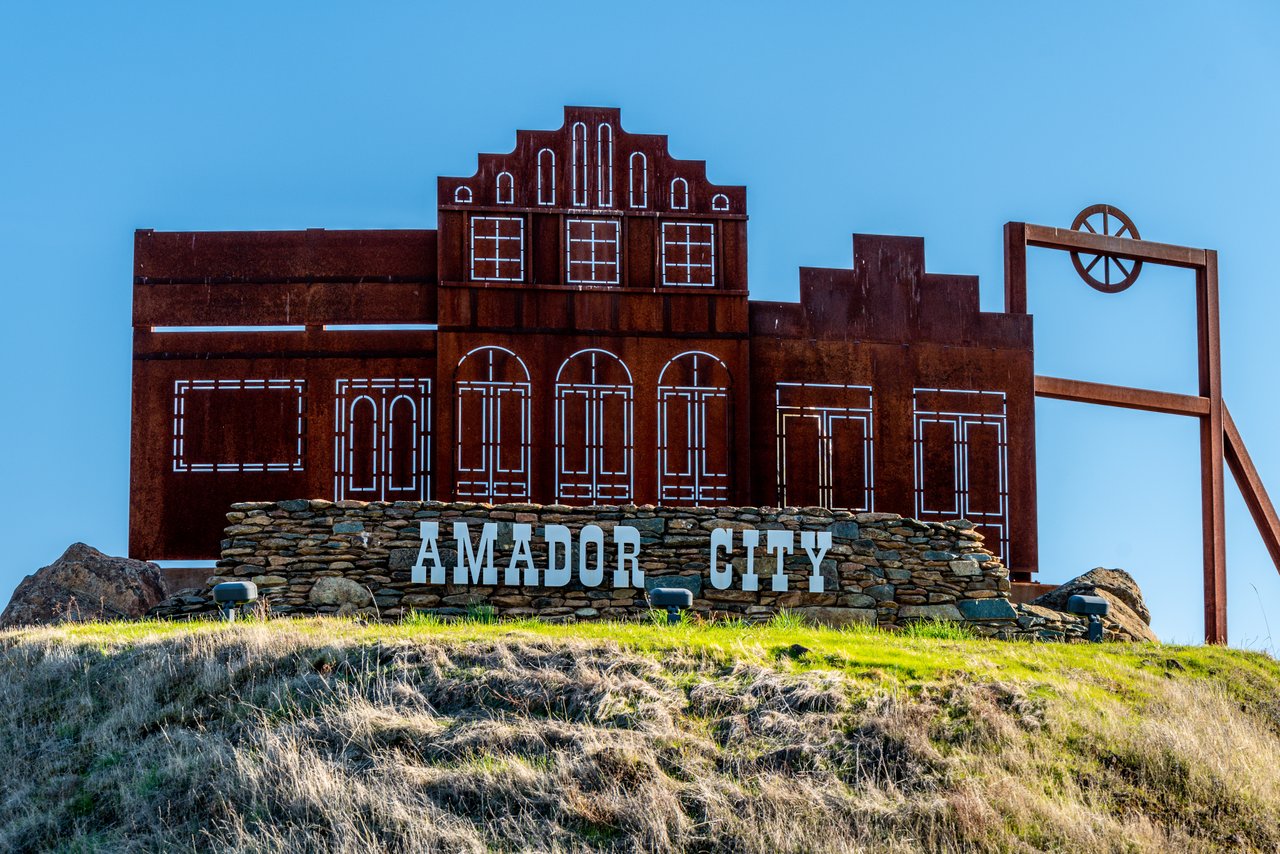 Amador City sign with a metal silhouette of historic storefronts on a grassy hillside.